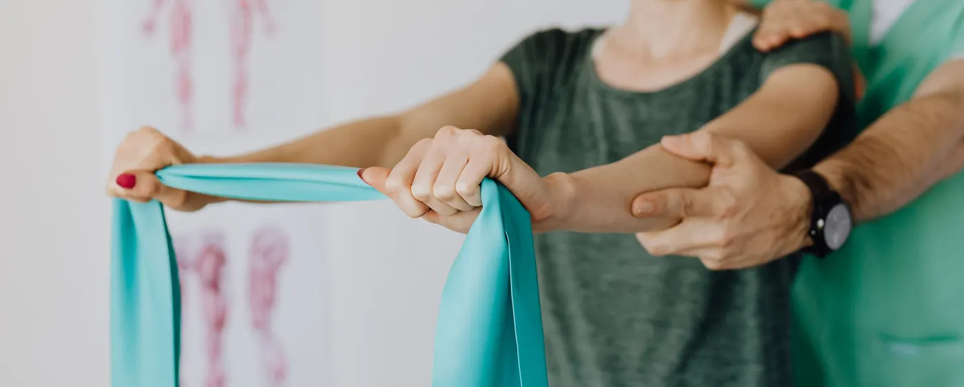 Therapeut führt die Arme einer Patientin bei einer Übung mit dem Theraband