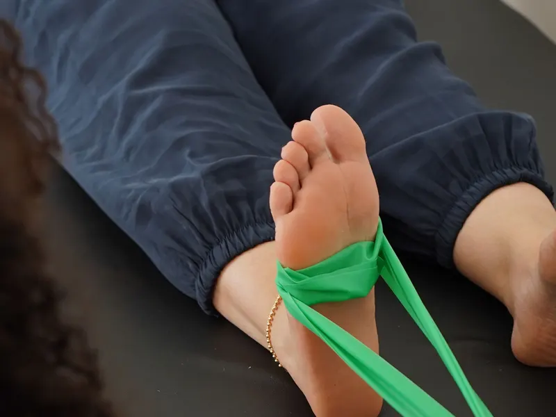 Fuß mit grünem Theraband auf der Behandlungsliege, Kräftigungsübung